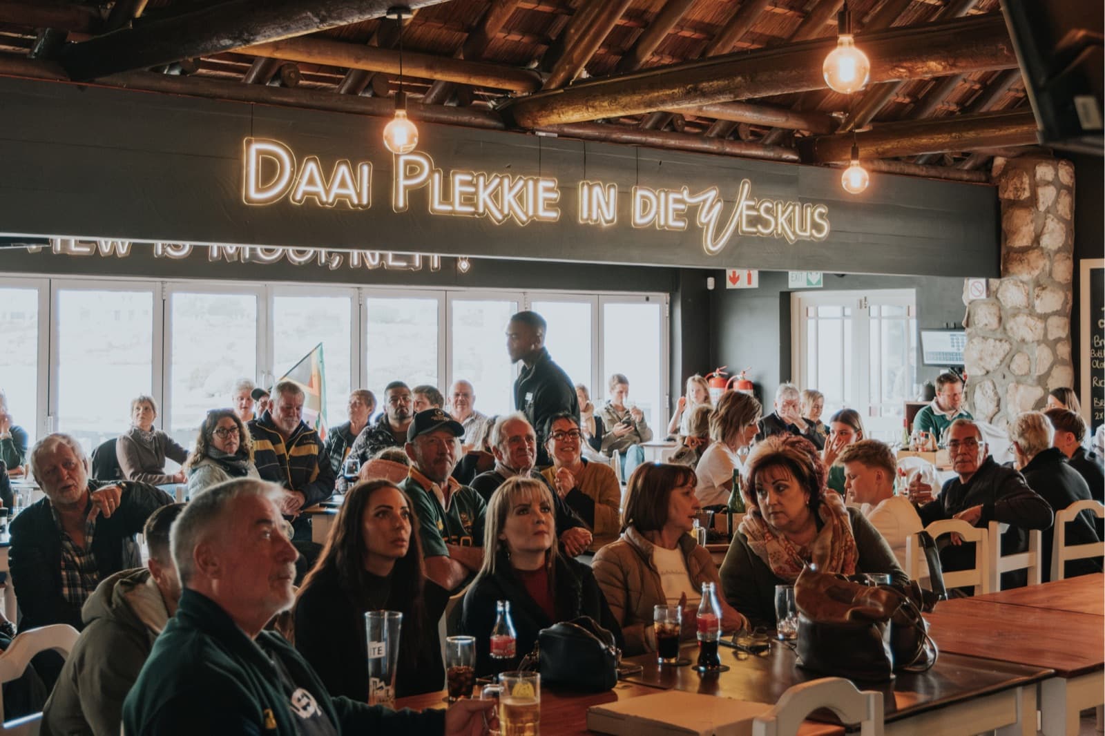 Rugby supporters under the Daai Plekkie in die Weskus neon sign